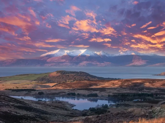 Scottish island landscape at sunset with snow-capped mountains across the water